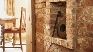 Una chimenea de ladrillo rústica con una puerta metálica, una silla de madera y una mesa al frente.