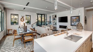 Cozinha moderna com ilha central, área de refeições e sala de estar com lareira e televisão.