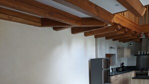 Une cuisine moderne avec des poutres en bois, un coin repas avec une longue table et des chaises, et un petit îlot central doté d’un évier.