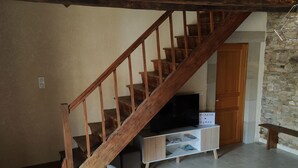 Un salon avec un escalier en bois, un téléviseur, un meuble blanc et deux canapés gris.