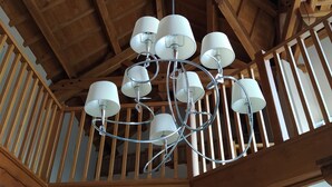 Un plafond en bois avec des poutres apparentes et un lustre orné de plusieurs abat-jours blancs.