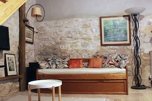 Una habitación con paredes de piedra, un sofá de madera, una mesita y una lámpara de pie.