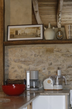 Una cocina con pared de piedra, un tazón rojo, una cafetera y una licuadora.