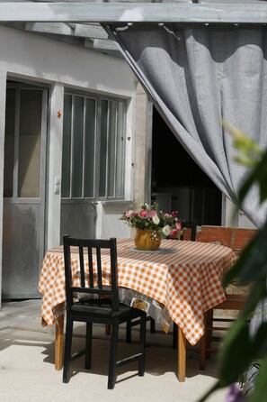 Un área de comedor al aire libre con una mesa cubierta por un mantel a cuadros, una silla y un jarrón con flores.