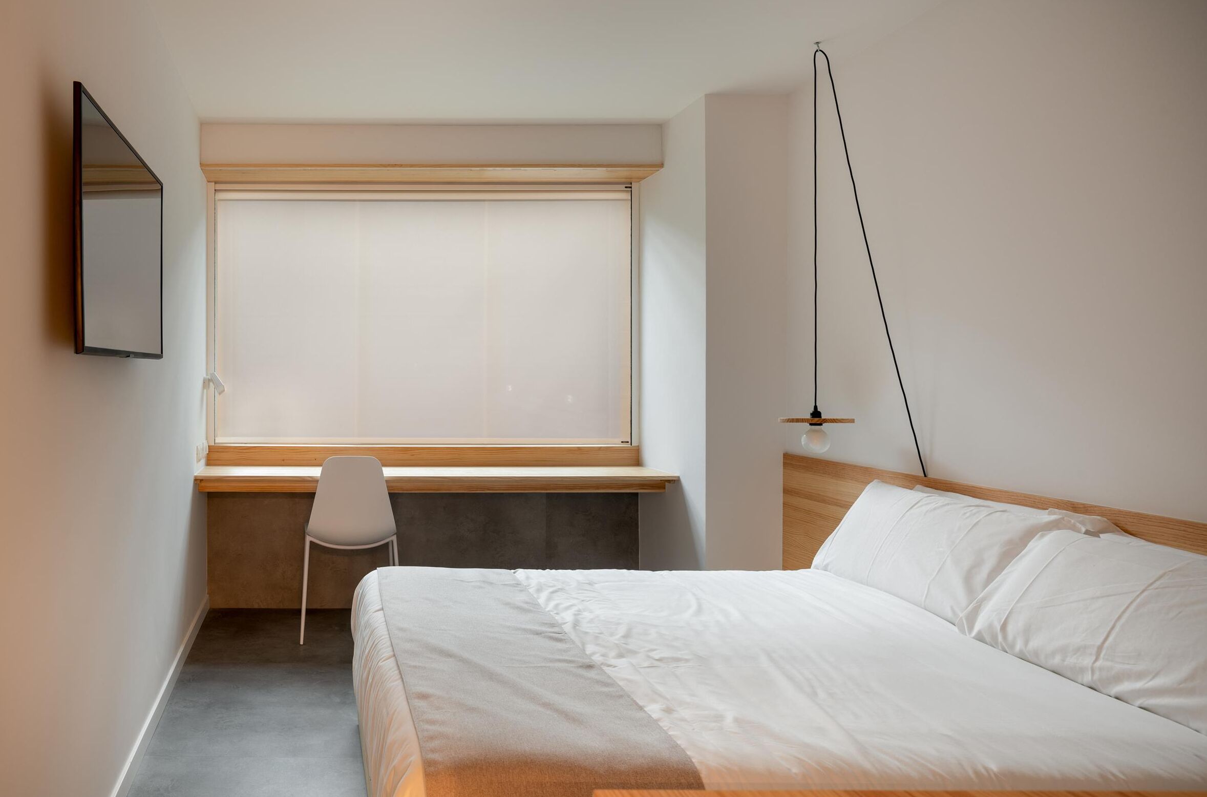 Un dormitorio con cama, un escritorio, una silla, una ventana con persianas y una lámpara colgante.