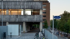 Um edifício moderno com entrada imponente, galeria coberta e placa indicando 