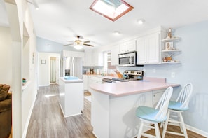 A modern kitchen with white cabinets, a central island, and a ceiling fan. - Pleasant beach home with central AC, deck & work space - walk to beach & dining (Tybee Island)