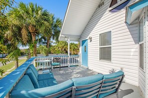 A covered patio with blue cushioned seating and a white railing, surrounded by palm trees. - Pleasant beach home with central AC, deck & work space - walk to beach & dining (Tybee Island)