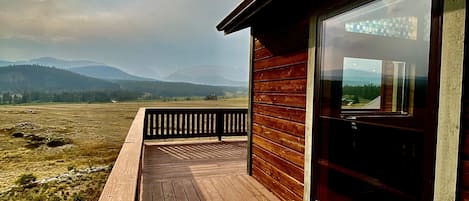 Une terrasse en bois qui mène à une porte vitrée donnant sur un paysage montagneux.