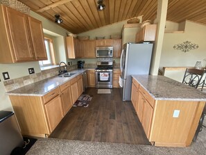 Une cuisine dotée de meubles en bois, de plans de travail en granit, d’appareils électroménagers en acier inoxydable et d’un plafond en bois.