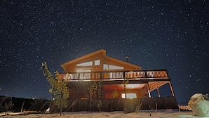A two-story wooden cabin with a balcony, set against a starry night sky. - The Gateway Cedar Lodge (Alma)
