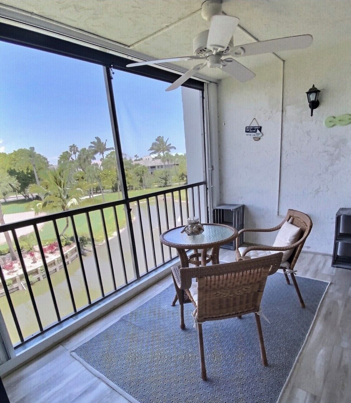 A balcony with a ceiling fan, a table with chairs, and a view of a park and buildings.