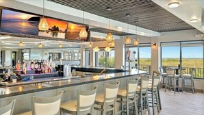 A modern bar area with a long counter, multiple seating options, and large windows offering scenic views. - Beach Condo in Hutchinson Island. Located in Ocean Village with Golf Course View (Hutchinson Island)