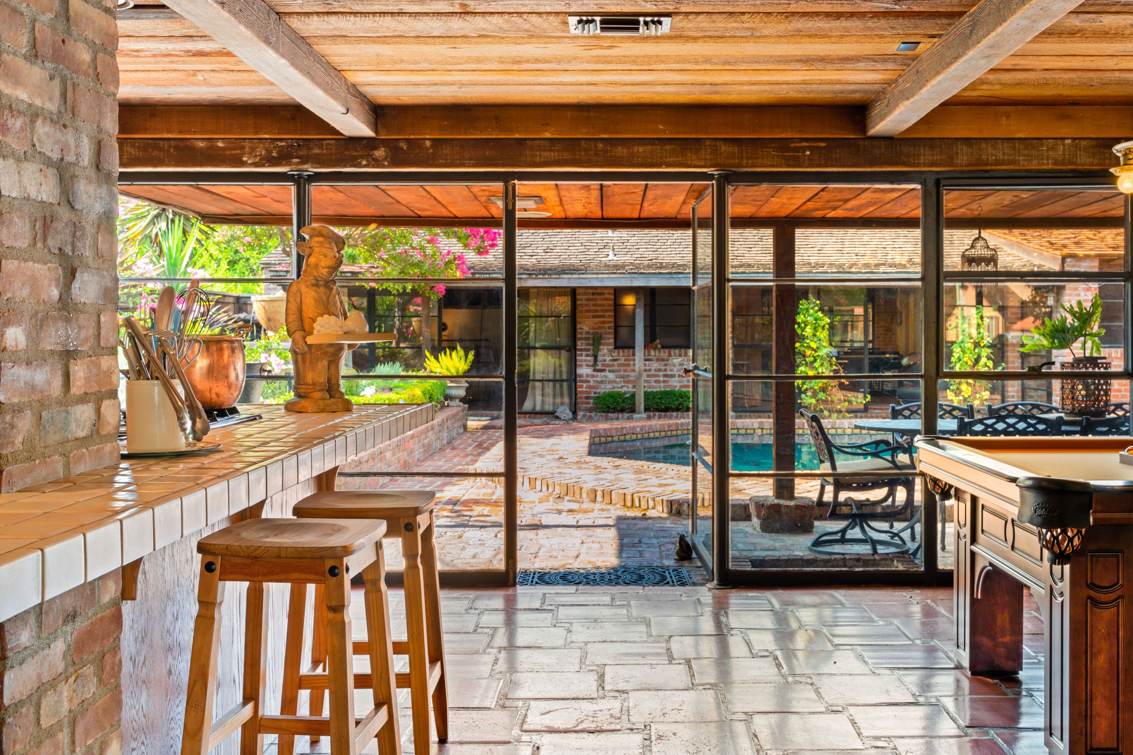 Un espace bar avec des tabourets, une table de billard et une vue sur un jardin, accessible par de grandes portes vitrées.