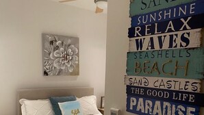 Une chambre à coucher comprenant un lit, des oreillers, une table de chevet, un ventilateur de plafond et un mur décoré de panneaux.