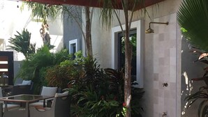 Une terrasse extérieure dotée d’un espace salon abrité, d’une petite table et de diverses plantes.