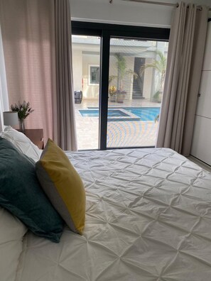 Ein Schlafzimmer mit Bett, Nachttisch und Blick auf einen Swimmingpool durch eine Glastür.