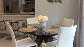 Un espace repas moderne avec une table en verre, des chaises blanches et un vase de fleurs.
