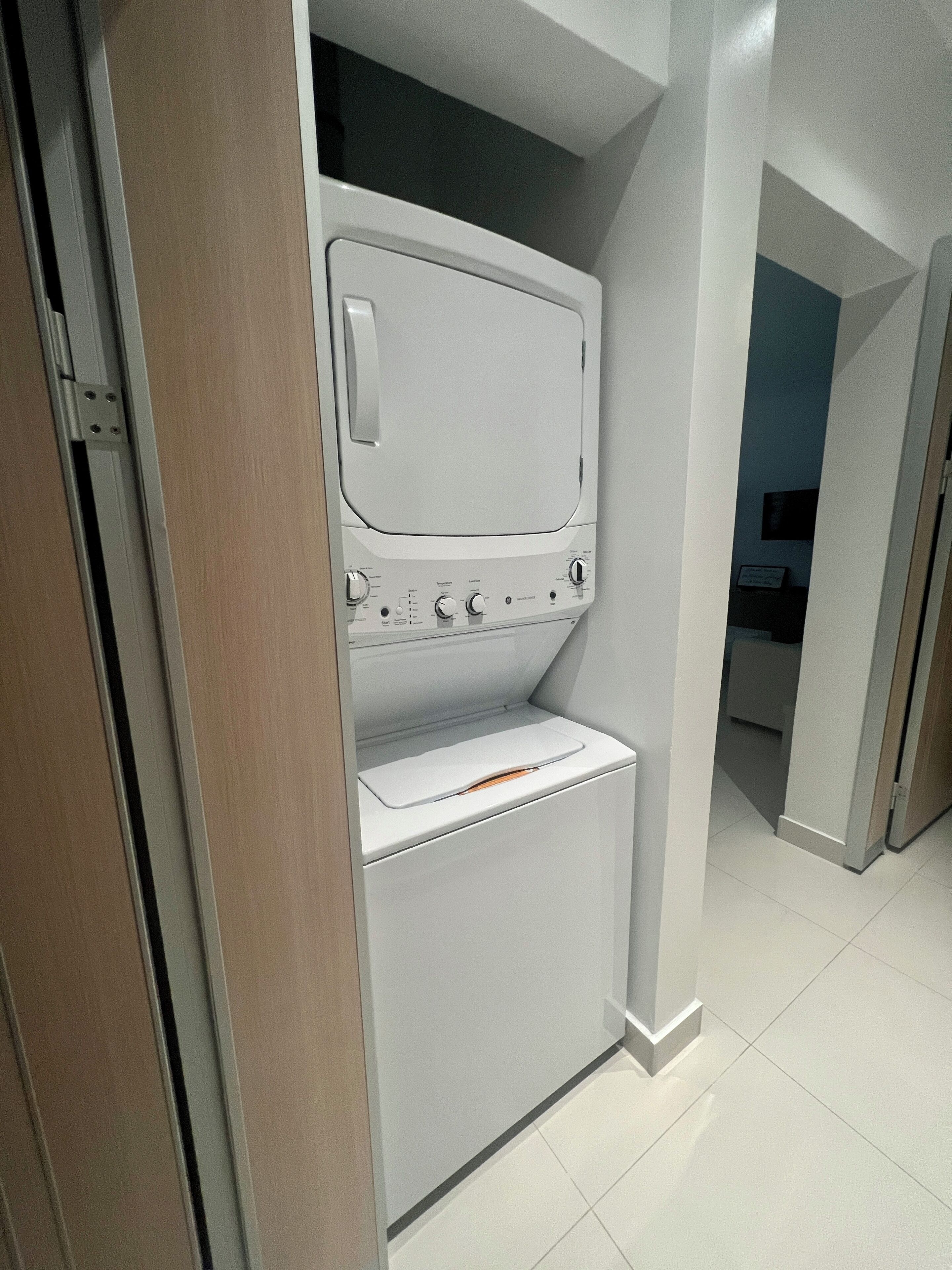 Un lavadero pequeño con lavadora y secadora, un marco de puerta de madera y piso de baldosas.