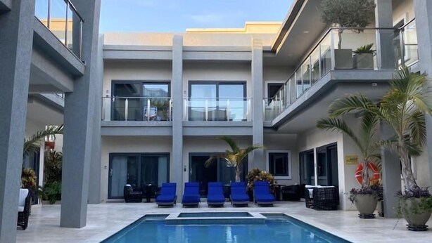 Un hôtel moderne doté d’une piscine centrale, de chaises longues bleues et d’un bâtiment à deux étages avec des balcons.