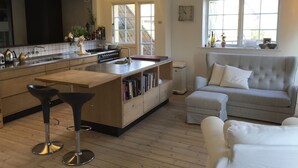 A modern kitchen with a central island, bar stools, a striped sofa, and a window with a view.