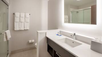 Un baño moderno con cabina de ducha de vidrio, un lavabo blanco con espejo y un perchero con varias toallas.