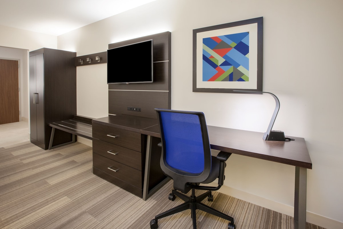 Un espace de bureau moderne comprenant un bureau, une chaise, un téléviseur et un tableau abstrait encadré.