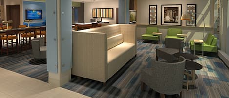 A hotel lobby with a sofa, chairs, a television, and artwork on the walls.