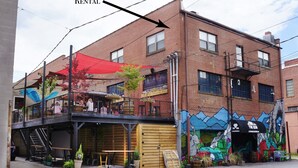 A two-story building with a ground-floor commercial space featuring outdoor seating and a mural. - Main Street Retreats 103 Brand New Downtown Apt 103 (Waynesville)