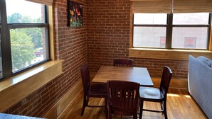 A dining area with a brick wall, wooden table, and chairs. - Main Street Retreats 103 Brand New Downtown Apt 103 (Waynesville)