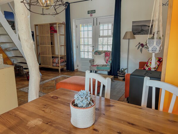 A cozy room with a wooden dining table, a chair, a sofa, a staircase, and a door with a sign.