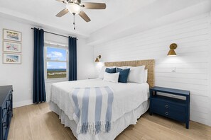 A bedroom with a bed, a nightstand, a ceiling fan, a window with curtains, and wall-mounted lights.
