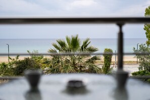 Une vue depuis une fenêtre donnant sur une plage bordée de palmiers, sous un ciel dégagé.