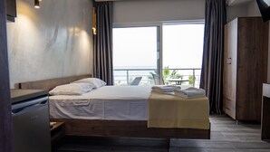 A modern hotel room with a bed, a small kitchenette, and a view of the sea.