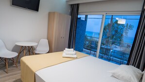 A hotel room with a bed, a small table, two chairs, a TV, and a balcony with a view.