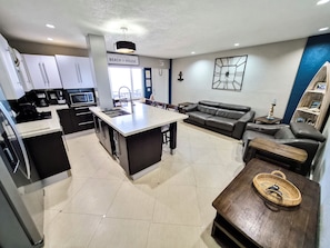 Uma cozinha moderna com uma ilha central, uma área de jantar com sofá e cadeiras, e uma sala de estar com um sofá e uma mesa de centro.