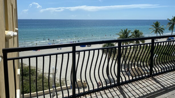 A balcony with a view of a beach, palm trees, and the ocean.