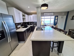 Cozinha moderna com ilha central, eletrodomésticos de aço inoxidável e vista para a praia.