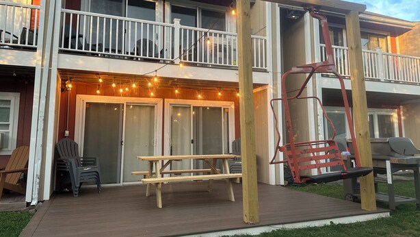 Een gebouw met twee verdiepingen, een houten terras, een schommel en lichtjes.