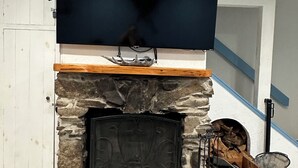Een woonkamer met een stenen openhaard, een wandgemonteerde flatscreen-tv en een houten plank boven de openhaard.