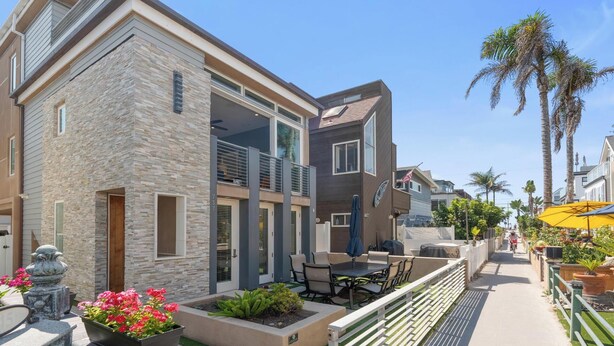 A modern two-story house with a stone facade, a balcony, and a patio with outdoor furniture. - Modern beach home only 8 houses from the beach. Check out our new drone video!! (San Diego)
