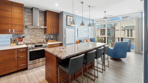 A modern kitchen with wooden cabinets, a large island with bar stools, and a view of the backyard. - Modern beach home only 8 houses from the beach. Check out our new drone video!! (San Diego)