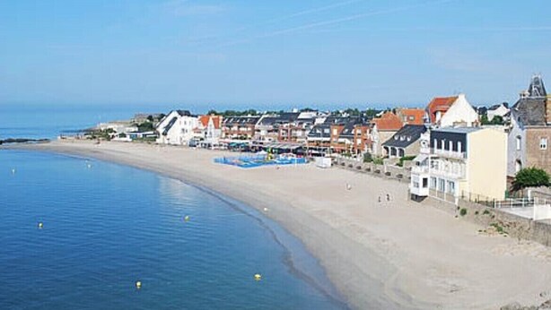 A coastal town with a sandy beach, buildings along the shore, and a calm sea.
