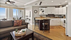 A modern kitchen with white cabinets, a dining area with a table and chairs, a living room with a sofa and a coffee table, and a ceiling fan.
