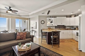 Une cuisine moderne avec des meubles blancs, un coin repas avec une table et des chaises, un salon avec un canapé et une table basse, et un ventilateur de plafond.
