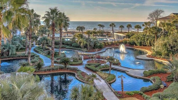 A resort with a large pool area, palm trees, and a view of the ocean.