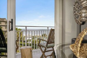 A balcony with a view of the beach, a wooden chair, and a woven chair.