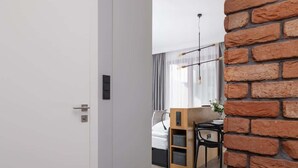Une chambre d’hôtel moderne avec un mur d’accent en briques, un bureau en bois, un lit avec une literie blanche et un luminaire suspendu.