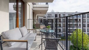 Un balcon avec un canapé, une table et des chaises. On aperçoit d’autres bâtiments en arrière-plan.