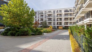 Un immeuble d’appartements moderne doté de nombreux balcons, d’une allée pavée et d’espaces paysagers agrémentés d’arbres et d’arbustes.